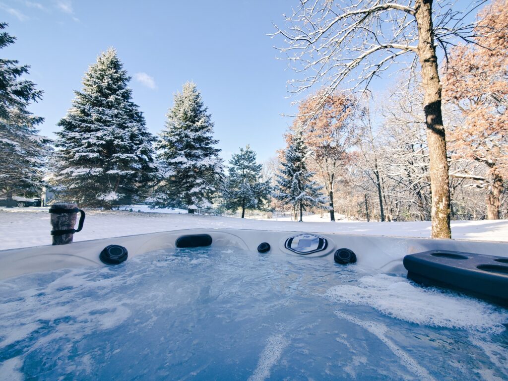 Outdoor hot tub in foreground with scenic background of snow covered pine trees.